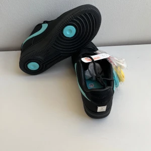 Nike Air Force 1 svart  - Säljer ett par svarta Nike Air Force 1 med och detaljer. Skorna har klassisk rund tå, platt sula och 3 extra skosnören i vitt,gult och blått 