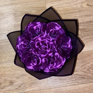 Bukett med lila rosor i tyg - En bukett med sju lila rosor gjorda av glansigt tyg, inslagna i svart transparent cellofan och knuten med ett lila sidenband. Perfekt som dekorativ accessoar eller present.