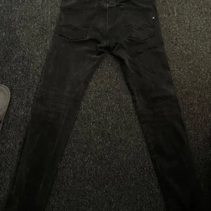 Svarta Replay jeansbyxor - Svarta jeansbyxor från Replay med klassisk femficksdesign och smal passform. Byxorna har dragkedja och knapp framtill samt diskret Replay-logga på bakfickan. Perfekta för en stilren look.