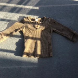 Beige ribbad långärmad tröja med knappar - Säljer en beige långärmad tröja i ribbat material med två knappar framtill vid halsen. Tröjan har en klassisk rund halsringning och är mjuk och skön, perfekt för lager-på-lager.