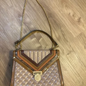 Quiltad axelväska från River Island - Säljer en quiltad axelväska från River Island med guldfärgade detaljer och kedjerem. Väskan har inslag av brunt och ormskinnsmönster samt ett stort RI-emblem framtill. Perfekt för dig som vill sticka ut med en snygg accessoar.