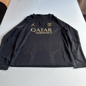Svart PSG fotbollströja med guldtryck från Jordan -  svart långärmad PSG fotbollströja från Jordan med guldiga detaljer och tryck. Alldrig använd med lapp fortfarande på, byxor finns till men är synbart använda skriv för mer info/ bilder. ÖPPEN FÖR BYTEN!