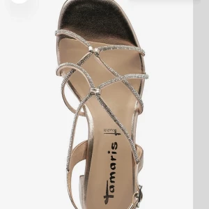 Guldiga sandaler med glittriga remmar från Tamaris - Säljer ett par klackar i guld/champangefärgade från Tamaris med glittriga remmar och låg klack. Skorna har öppen tå och justerbart spänne vid ankeln. Utgångspris 900!