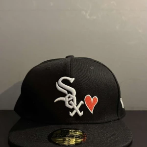 New Era keps - Tjabba!! Säljer denna riktigt frächa New Era kepsen med en riktigt exklusivt design! Kepsen har en  klassisk vit ”chicago white sox” logga på framsidan. Två broderade matchande hjärtan fins på både framsida och baksida vilket gör den unik mot den klassiska  ”white sox” kepsen. Sjukt snygg nu i sommar!! Det fins inga fula märken eller liknade, utan kepsen är som NY! Alla klistermärken är kvar om man gillar de;) hör gärna av dig. Storleken är: 7-3/8 (58,7cm) 