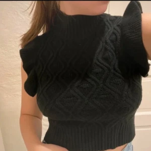 Svart stickad polotopp från SHEIN - Svart stickad polotopp från SHEIN i storlek S. Toppen har ett snyggt kabelstickat mönster, höga ribbade kanter och markerade axlar utan ärmar. Perfekt för dig som gillar trendiga och bekväma plagg med lite edge.