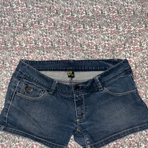 Mörkblå jeansshorts från Lois - Snygga mörkblå jeansshorts från Lois med klassisk femficksdesign, coola detaljer på bakfickorna och kontrastsömmar. Shortsen har låg midja. Perfekta för sommardagar och festivalhäng.