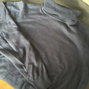 Mörkblå polotröja i stickad bomull - Snygg mörkblå polotröja med klassisk ribbad krage och långa ärmar. Tröjan är stickad i mjuk bomull och passar perfekt för lager-på-lager under kyliga dagar. Enkel och stilren design som funkar till det mesta.