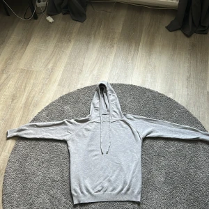 Ljusgrå hoodie med luva  och snörning - En stilren ljusgrå Marinollull hoodie med luva  och snörning. Tröjan har långa ärmar och ribbade muddar vid ärmslut och nederkant. Perfekt för en chill och avslappnad look. Tillverkad i mjuk bomullsmix som känns skön mot huden.