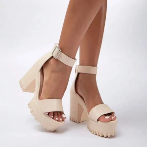 Beige sandaler med klack 38 - Snygga beige sandaler med hög klack och grov sula. De har en justerbar rem runt ankeln med ett metallspänne. Perfekta för sommarens alla fester och tillfällen när du vill känna dig extra chic. De är både bekväma och trendiga, vilket gör dem till ett måste i garderoben!