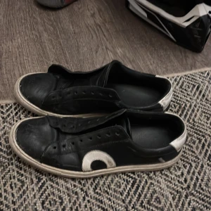 Svarta sneakers från Oliver Cabell - Svarta sneakers från Oliver Cabell med vita detaljer och rund tå. Skorna har en vit sula och en stor vit cirkel på sidan samt vit hälkappa med logga. Tillverkade i skinn och med klassisk snörning. Perfekta för dig som gillar stilrena och unika sneakers. Menning med modell är att de ska se lite smutsigt ut, men den är lite sönder som du kan se på sista bilden och det är därför jag säljer dem så billigt, priset är inte hugget i sten!