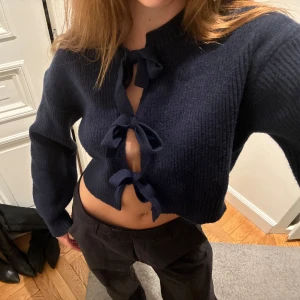 Mörkblå kofta med rosetter - Superfin mörkblå kofta med tre stora knyt framtill. Tröjan är stickad och har långa ärmar. Perfekt för dig som gillar trendiga detaljer och vill ha en mysig men ändå snygg look! XS men passar som S också