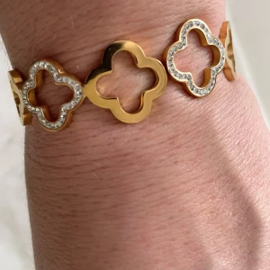 Guldigt armband med fyrklöver och stenar - Snyggt armband i guldton med flera fyrklöverformade länkar, vissa dekorerade med glittrande stenar. Armbandet har en unik låsdetalj och ger en lyxig känsla. Perfekt för dig som gillar statement-smycken och vill sticka ut. Passar 17-18cm ( jag har 18 så det är max )