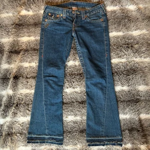 True Religion bootcut jeans - Säljer ett par snygga, klassiska, low waist jeans från True Religion med bootcut passform. Jeansen har dekorativa bakfickor med knappar och en glitterdetalj på höger framsida. Storlek W27, beninnerlängd 74 cm 💕💕💕💕