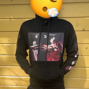 Off-White svart hoodie med konstmotiv - Svart hoodie från Off-White med ikoniskt konstmotiv på bröstet och stora röda pilar på ryggen. Har snörning i huvan och tryckta detaljer längs ärmarna. Perfekt för dig som vill sticka ut med streetwear vibes. Passar mig som är 175 cm lång och väger ca 72 kg 