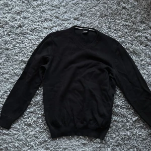 Svart stickad tröja från BOSS - Svart stickad tröja från BOSS i storlek M. Tröjan har v-ringad halsringning och är tillverkad av fin italiensk ull. Klassisk och stilren modell med långa ärmar och ribbade muddar. Perfekt för dig som gillar en clean och tidlös look. Lite mindre än M känns mer som en S