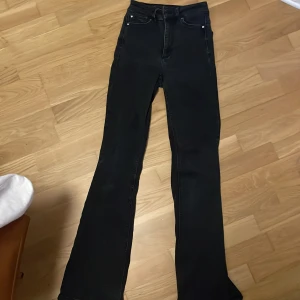 Svarta bootcut jeans med hög midja - Snygga svarta jeans med bootcut-modell och hög midja. Klassisk femficksdesign och bälteshällor. Jeansen har en mörk tvätt och är tillverkade i stretchigt denim för en bekväm passform. Perfekta till sneakers eller boots. de är urtvättade 