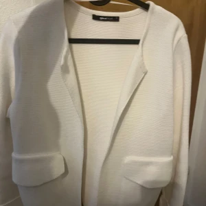 Vit cardigan jacka från Gina Tricot - Snygg vit cardigan jacka från Gina Tricot med stilren design. Jackan har långa ärmar, två fickor framtill och är tillverkad i ett mjukt, stickat material. 