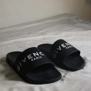 Svarta Givenchy slides  - Snygga svarta slides från Givenchy med vit logotyp på ovandelen. Perfekta inför sommaren eller om du ska utomlands. Tillverkade i syntetmaterial för bekvämligheten och hållbarheten. 
