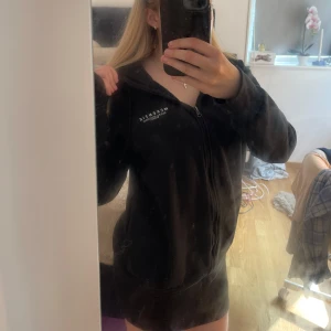 Svart zip-hoodie från McKenzie - Svart hoodie med dragkedja från McKenzie, har huva med snörning. Mjuk insida och enkel logga på bröstet. Perfekt för kyligare dagar/kvällar eller när du vill ha en enkel och skön look.