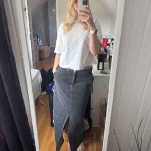 Svart lång jeanskjol med slits från NAKD - Säljer en svart/mörkgrå lång jeanskjol med slits framtill och bak. Perfekt till sommaren och passar till alla slags outfits! Jag är 174 cm och den är lång på mig🥰