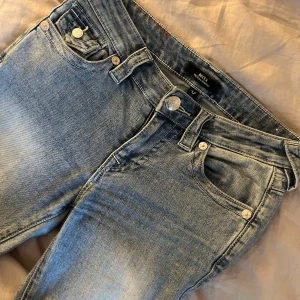 True Religion Becca Bootcut Jeans ljusblå - Ljusblå jeans från True Religion, modell Becca Mid Rise Bootcut. Klassisk femficksdesign med snygga detaljer och logga på bakfickan. Jeansen har bootcut-snitt och är tillverkade i mjukt denimtyg för en skön passform. Använd några gånger och lite slitna vid hälarna men annars jättebra skick, en av bakfickorna har knappen ramlat av på också, pris går att diskutera💕