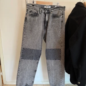 Grå patchade jeans från Our Legacy - Säljer ett par grå jeans från Our Legacy med coola mörkare patch-detaljer över knäna. Jeansen har rak passform, klassisk femficksdesign och är tillverkade i 100% bomull. Perfekta för dig som gillar en unik och avslappnad stil.