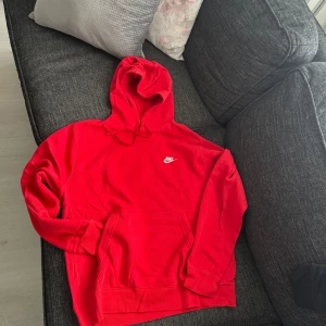 Röd Nike hoodie med huva - Säljer en röd hoodie från Nike med klassisk vit logga på bröstet. Tröjan har huva med snörning och en stor magficka framtill. Perfekt för dig som gillar sportig och avslappnad stil. Passar folk med storlek S och M