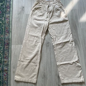 Beiga wide kostymbyxor från MNG - Snygga beiga kostymbyxor från MNG med breda ben och hög midja. Byxorna har hällor för bälte, snedställda fickor fram och dekorativa fickor bak. Perfekta för en clean och stilren look.