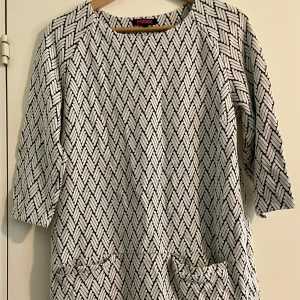 Svartvit Mönstrad klänning från Indiska i stl L - Snygg svartvit kortare klänning från Indiska med grafiskt mönster och trekvartsärm. Modellen är rak och har två fickor framtill. Materialet är en mix av bomull, polyester och lite elastan för extra komfort, lite tjockare tyg, normal i stl. Använd fåtal ggr, inget att anmärka på.