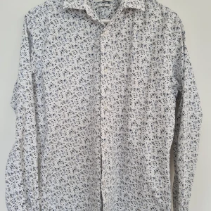 Småblommig skjorta från Jack & Jones - Vit långärmad skjorta från Jack & Jones med småblommigt mönster i blått och brunt. Passform Slim, storlek Large.  Mycket fint skick, använd någon enstaka gång.