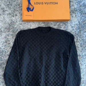 Svart stickad tröja Louis Vuitton M - Exklusiv svart stickad tröja från Louis Vuitton med unik vävd struktur och diskret metallogo. Tröjan har rund halsringning och långa ärmar, perfekt för dig som vill ha en stilren och lyxig look. Tillverkad i Italien och känns riktigt premium.