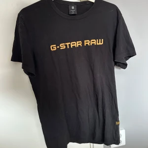 Svart G-Star Raw t-shirt med tryck - Svart t-shirt från G-Star Raw med klassiskt gult logotryck över bröstet. Enkel och stilren design med rund hals och korta ärmar. Perfekt för dig som gillar streetwear och vill ha en basic tee med snygg branding.