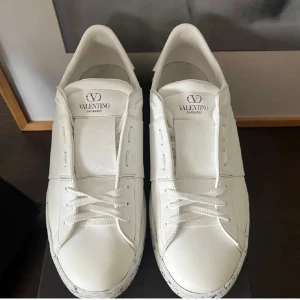 Valentino Garavani vita sneakers - Snygga vita sneakers från Valentino Garavani med stilren design och coola nitar baktill. Skorna har snörning, rund tå och en vit sula med svarta stänkdetaljer. Tillverkade i skinn för en lyxig känsla och passar perfekt till streetwear eller en clean look. Priset går att diskutera. Storlek 43, skriv om ni har frågor 