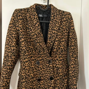 Leopardmönstrad kavaj från Zara XS - Snygg kavaj från Zara i leopardmönster med dubbelknäppning och markerad krage. Färgerna är brun och svart, perfekt för dig som vill sticka ut. Kavajen har långa ärmar och är tillverkad i ett mjukt material med fodrad insida.