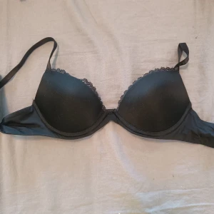 Svart push-up bh från Calvin Klein - Svart push-up bh från Calvin Klein med tunna axelband och lätt vadderade kupor. Ovanpå kuporna finns en fin spetskant som ger en extra snygg detalj. Bh:n har klassisk form och är riktigt bekväm för dig som vill ha en stilren look.