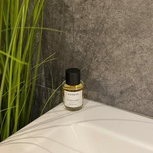 ESSNCE Sassy Classy Eau de Parfum - En stilren parfymflaska i glas med svart lock och vit etikett. ESSNCE Sassy Classy Eau de Parfum har en fräsch och modern look, perfekt att ha framme på badrumshyllan. Flaskan är rund och genomskinlig med ljusgul vätska inuti.