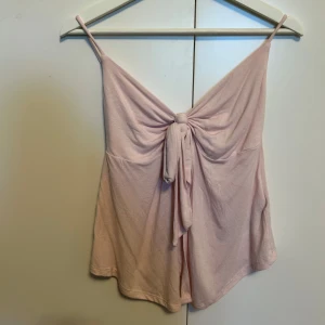 Ljusrosa linnetopp från Gina Tricot - Supersöt ljusrosa linnetopp från Gina Tricot med smala axelband och snygg knytning framtill. Toppen har en flowy passform och är perfekt för varma dagar. Mjuk och skön känsla, enkel att styla med jeans eller kjol.
