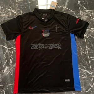 FC Barcelona Lamine Yamal svart matchtröja - Snygg svart FC Barcelona fotbollströja från Nike med Lamine Yamal och nummer 19 på ryggen. Tröjan har röda och blå sidopaneler, klubbmärke på bröstet och Cactus Jack-tryck framtill. Tillverkad i lätt och ventilerande material, perfekt för match eller träning.