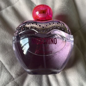Moschino Pink Bouquet parfym - Moschino Pink Bouquet parfym i en hjärtformad glasflaska med ljusrosa nyans. Flaskan har en glittrig silverdekor upptill och ett knallrosa lock med rosett. Perfekt för dig som gillar söta och lekfulla dofter och snygg design på sminkbordet.