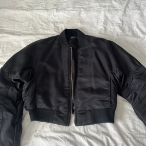 Svart bomberjacka från Gina Tricot - Säljer en svart bomberjacka från Gina Tricot i storlek S. Jackan är croppad med ribbade muddar vid ärmslut och midja, har dragkedja framtill och klassisk bomberkrage. Perfekt för dig som vill ha en stilren och trendig look.