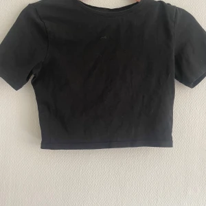 Svart croppad t-shirt - En enkel svart croppad t-shirt med korta ärmar och rund halsringning. Perfekt att matcha med höga jeans eller kjol för en avslappnad stil.