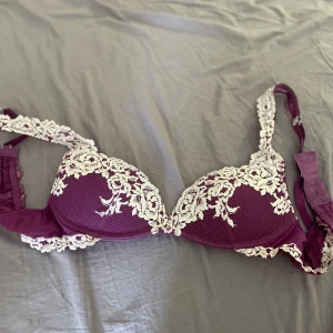 Lila spets-bh från intimismi 70 B  - Säljer en lila bh med vackra vita spets- och broderade detaljer. Bh:n har vadderade kupor och justerbara axelband. Perfekt för dig som vill ha något både snyggt och bekvämt under kläderna.
