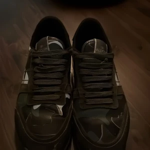 Valentino Rockrunner sneakers med camouflage - Säljer ett par Valentino Rockrunner sneakers i grönt och svart med camouflage-mönster. Skorna har snörning, rund tå och detaljer i skinn och syntet. Klassisk Valentino-logga på plösen och nitar på hälen. Bara skorna hänger med. Pris kan diskuteras!