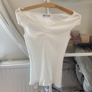 Vit v-ringad topp från Zara - Säljer en vit, croppad topp från Zara med v-ringning och lätt rynkad struktur. Toppen är tight men materialet är ändånlite stretchigt. Perfekt för varma dagar eller att styla lager på lager. Säljer då jag tycker att den inte klär mig. 