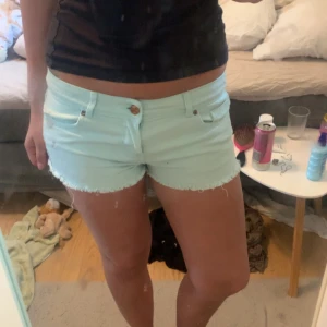 Ljusblå jeansshorts från Denim Co. - Säljer ett par ljusblå jeansshorts från Denim Co. med fransad kant och klassisk femficksdesign. Shortsen har låg midja och stängs med knapp och dragkedja. Perfekta för varma dagar och enkel att matcha med olika toppar.