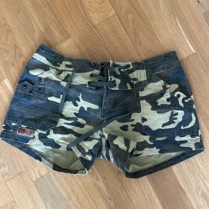 Camo shorts med snörning från Sky - Snygga camouflagemönstrade shorts från Sky med snörning framtill och coola metalldetaljer. Shortsen har låg midja och är perfekta för en avslappnad stil. Billabong-tryck baktill ger extra edge. (Mindre i storlek) Skriv till mig vid intresse! 