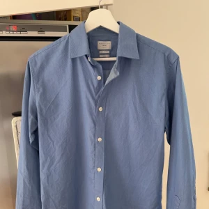 Blå skjorta från Selected Homme - Säljer en stilren blå skjorta från Selected Homme i slim fit-modell. Skjortan har klassisk krage, knäppning framtill och är tillverkad i ett lättskött bomullstyg som är enkel att stryka. Perfekt för dig som gillar en clean look.