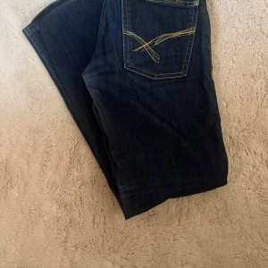 Lowwaist vintage jeans - Säljer ett par mörkblå jeansbyxor från Denimdivas med kontrasterande gula sömmar och snygg broderad bakficka. Vintage, storlek 26/32 men är korta i längden 