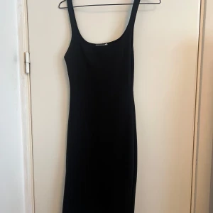 Svart tight klänning med slits - En svart, tight klänning med smala axelband och slits baktill. Klänningen har en enkel och stilren design som passar perfekt till många tillfällen. Materialet känns mjukt och stretchigt.