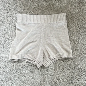 Beige stickade shorts med ribbad midja - Superfina beige stickade shorts med bred ribbad midja och ribbade kanter nertill. Mjukt material och skön passform, perfekta för en avslappnad look.